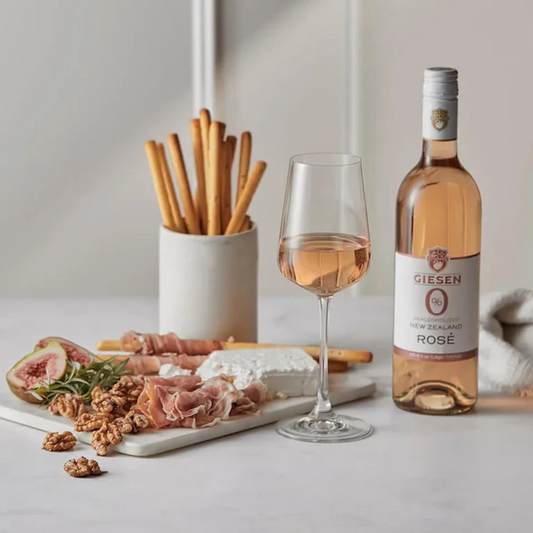 Bottle of Giesen Rosé wine with a glass of wine and charcuterie board on a light surface.