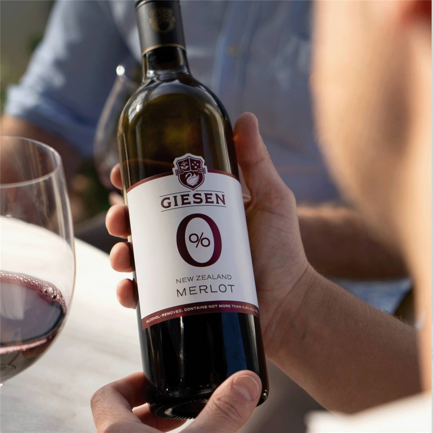 Bottle of Giesen 0% New Zealand Merlot wine held by a person with a blurred background