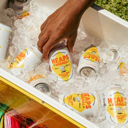 Hand reaching into a cooler filled with ice and 'Heaps Normal' beer bottles.
