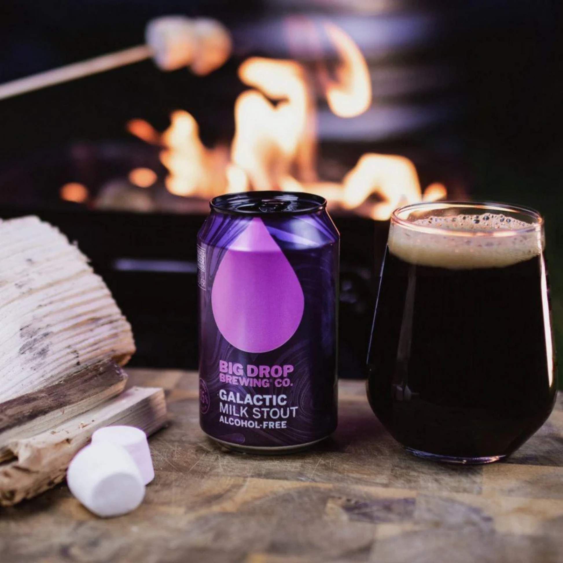 Big Drop Brewing Co. Galactic Milk Stout can and glass on a table with a fire in the background