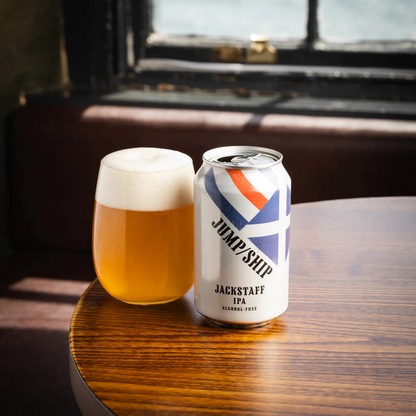 Can of Jackstaff IPA and glass of beer on a wooden table with a window in the background