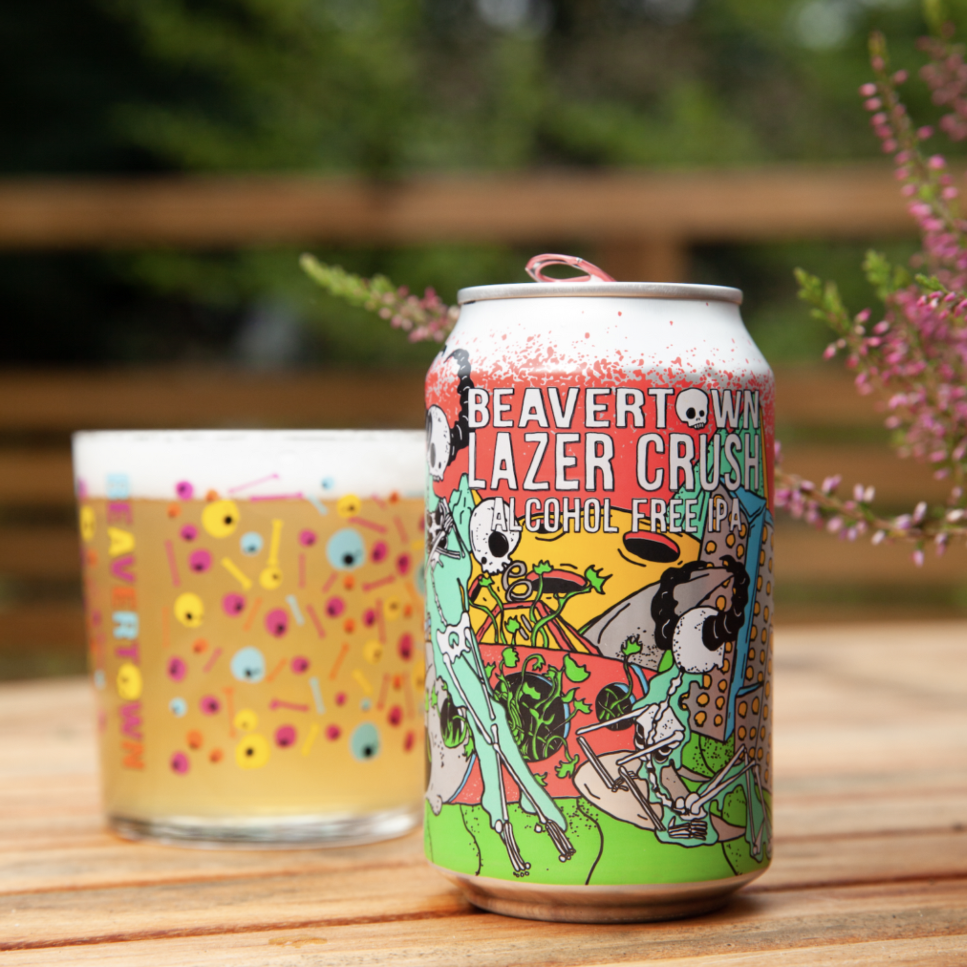 Beavertown Lazer Crush alcohol-free IPA can with a glass of beer on a wooden surface outdoors.