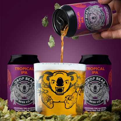 Drop Bear Beer Co. Tropical IPA being poured into a glass with beer cans around on a purple background