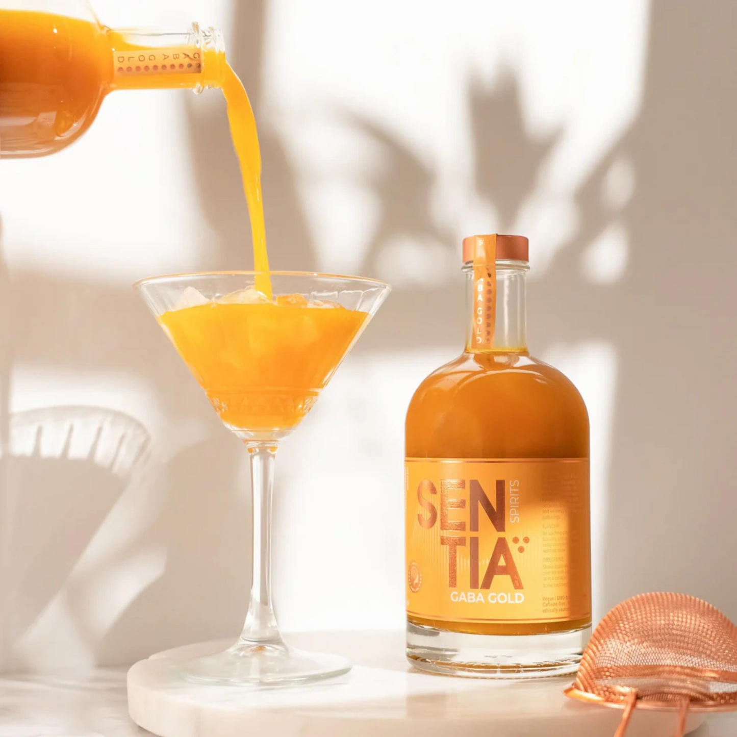 Orange liquid being poured into a glass with a bottle labeled 'SentiA' in the background.