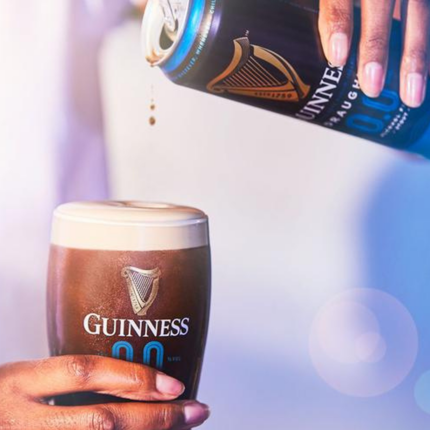 Person pouring Guinness beer from a can into a glass with a blurred background