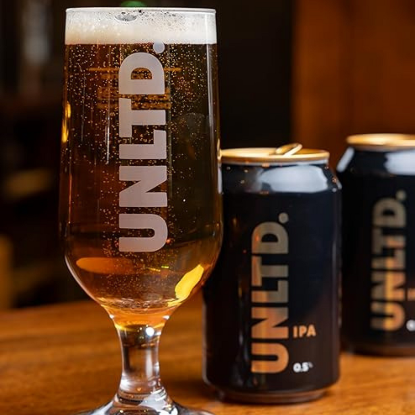 UNLTD. beer glass and cans on a wooden surface with a blurred background
