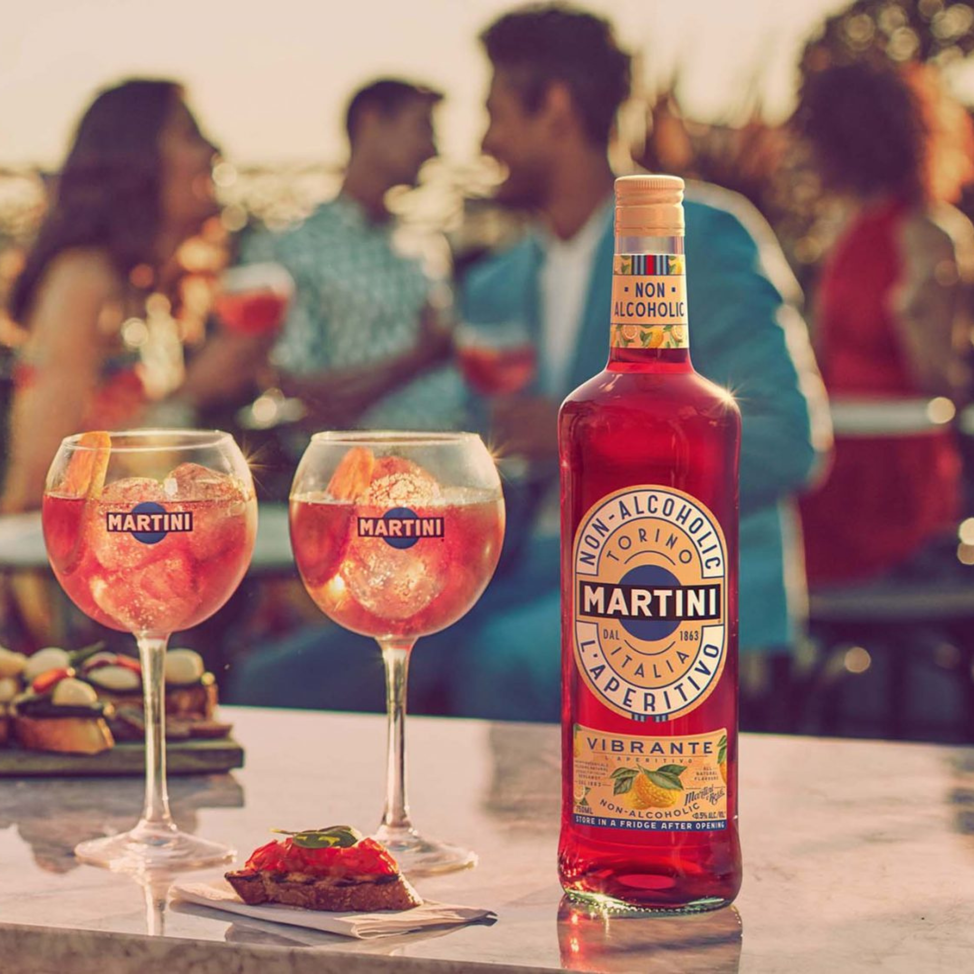Non-alcoholic Martini bottle with two glasses of pink cocktail on a table outdoors.