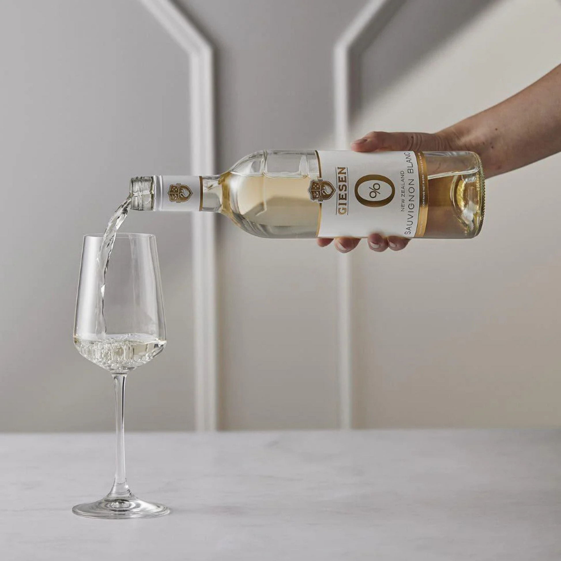 Bottle of wine being poured into a glass with a neutral background