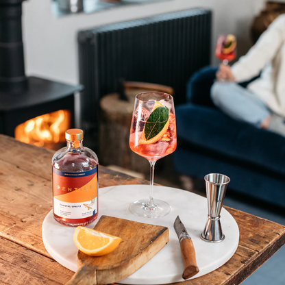 Bottle of PENT and a cocktail with orange slices on a marble tray in a cozy living room.
