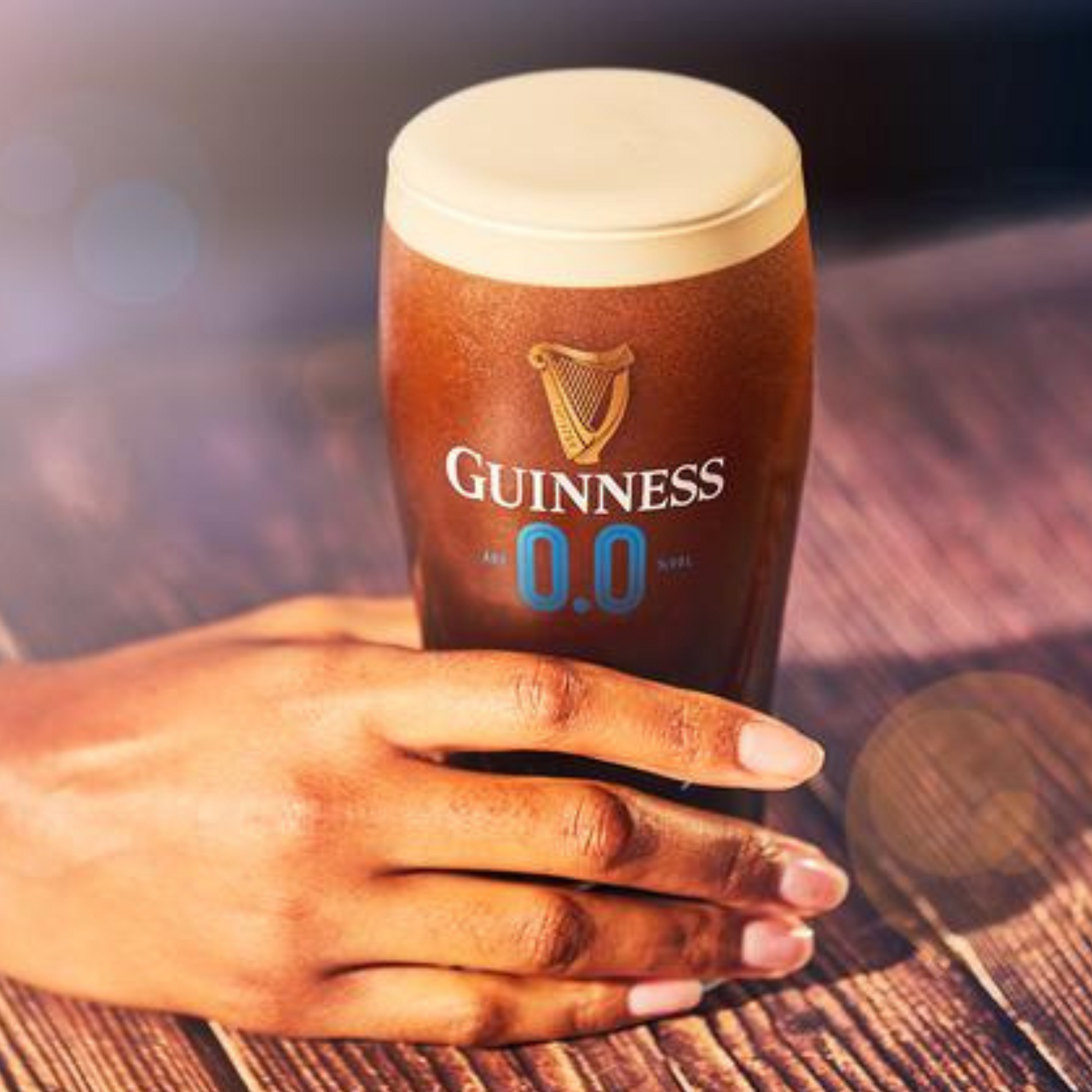 Hand holding a glass of Guinness 0.0 on a wooden surface