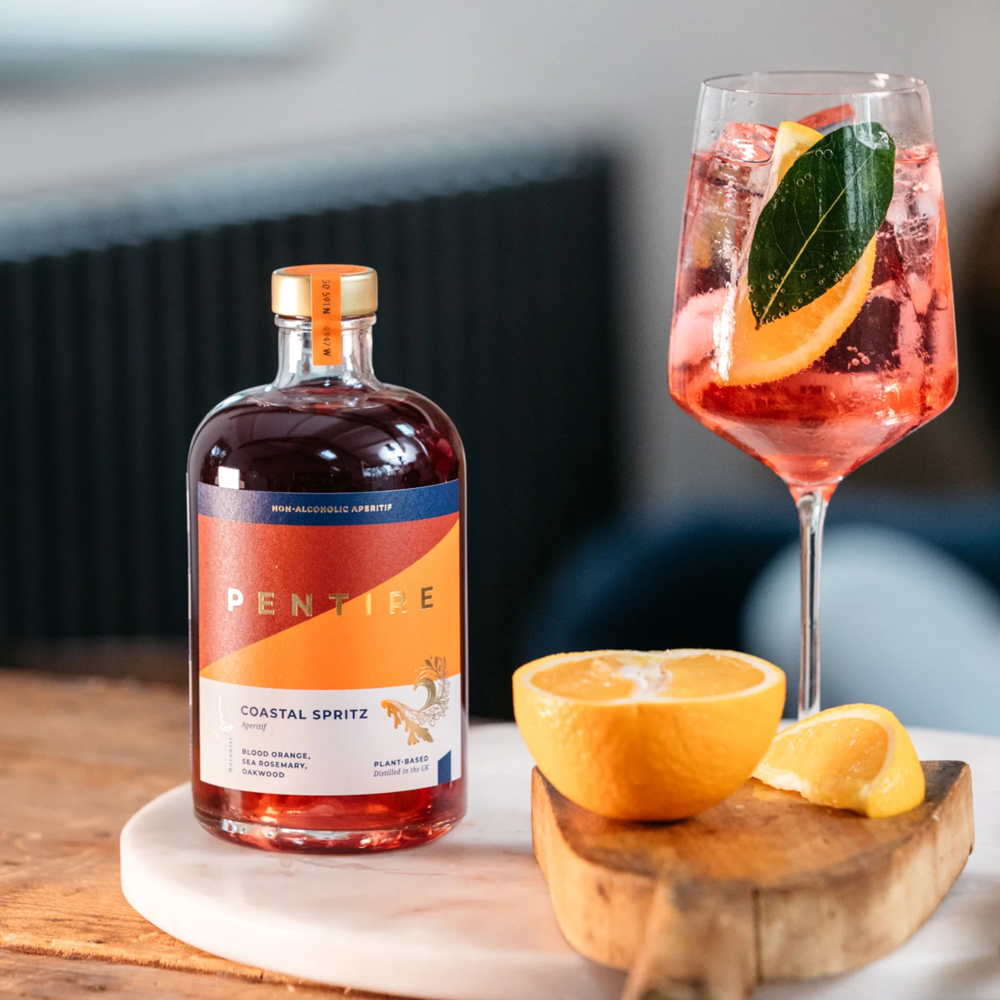Bottle of Pentipe Coastal Spritz with a glass of spritz and orange slices on a wooden board.