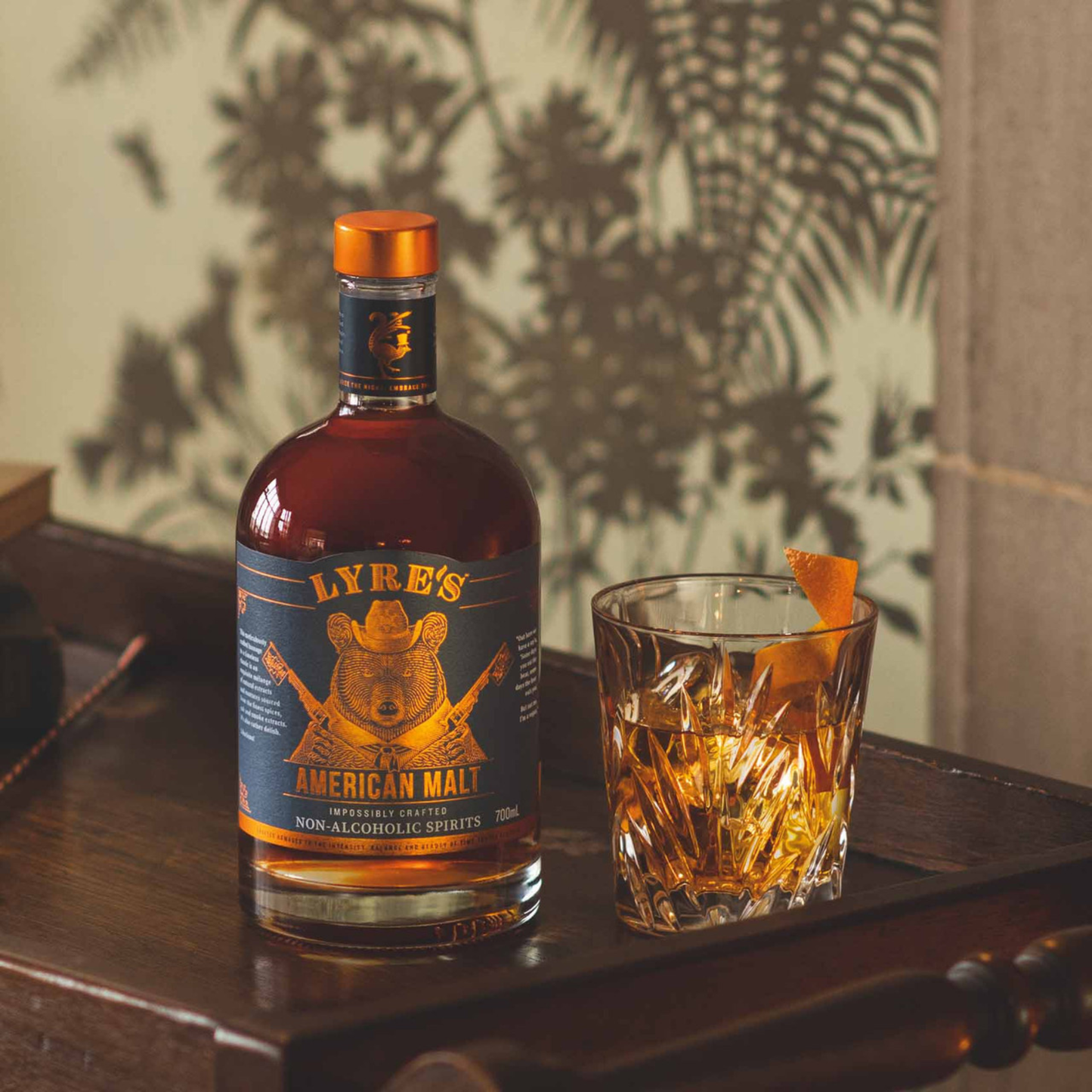 Bottle of Lyre's American Malt non-alcoholic spirits with a glass of amber liquid on a wooden surface.