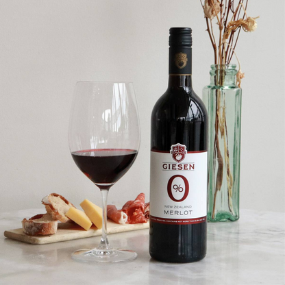 Bottle of Giesen 0% Merlot wine with a glass of wine and appetizers on a table.