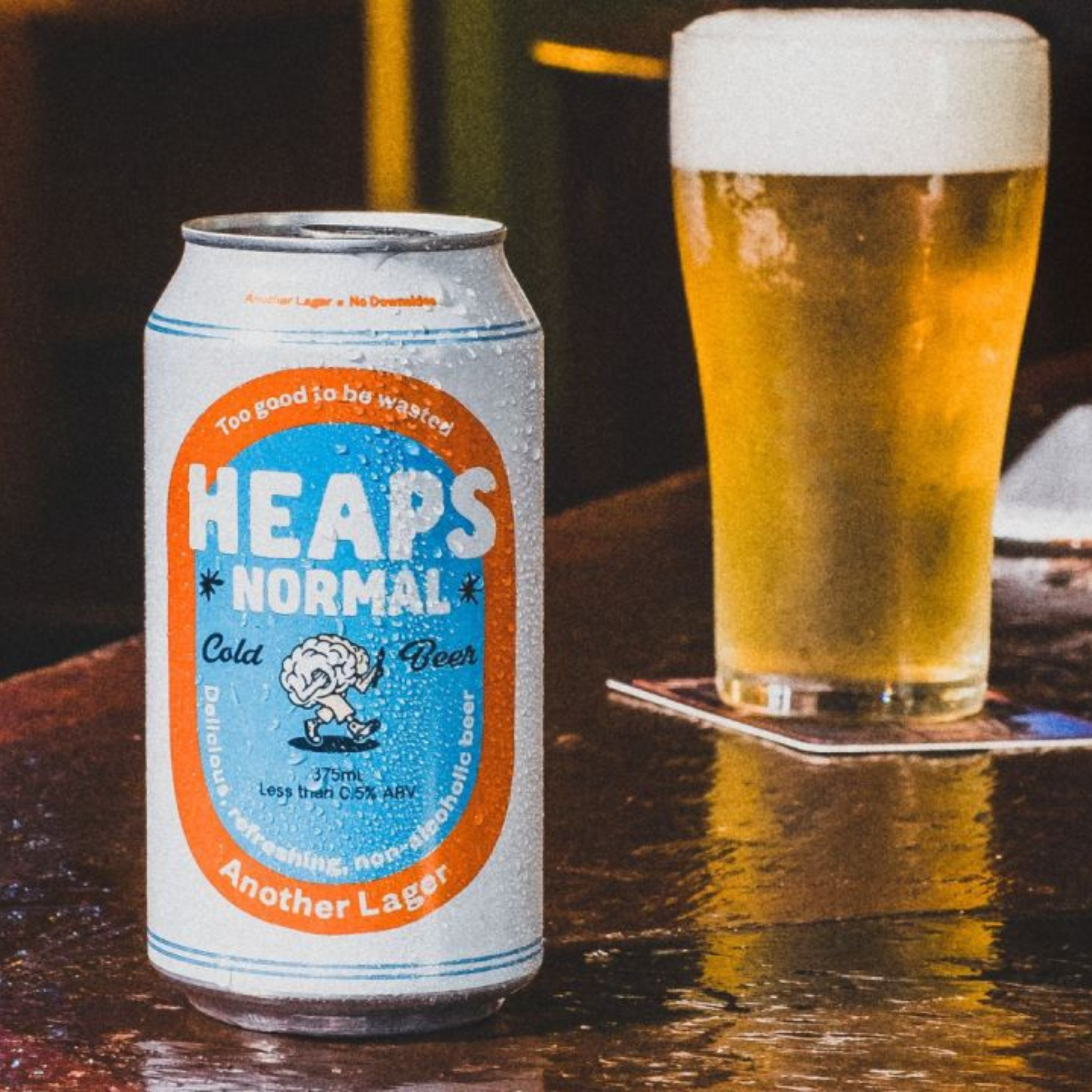 Can of 'Heaps Normal' beer next to a glass of beer on a wooden surface