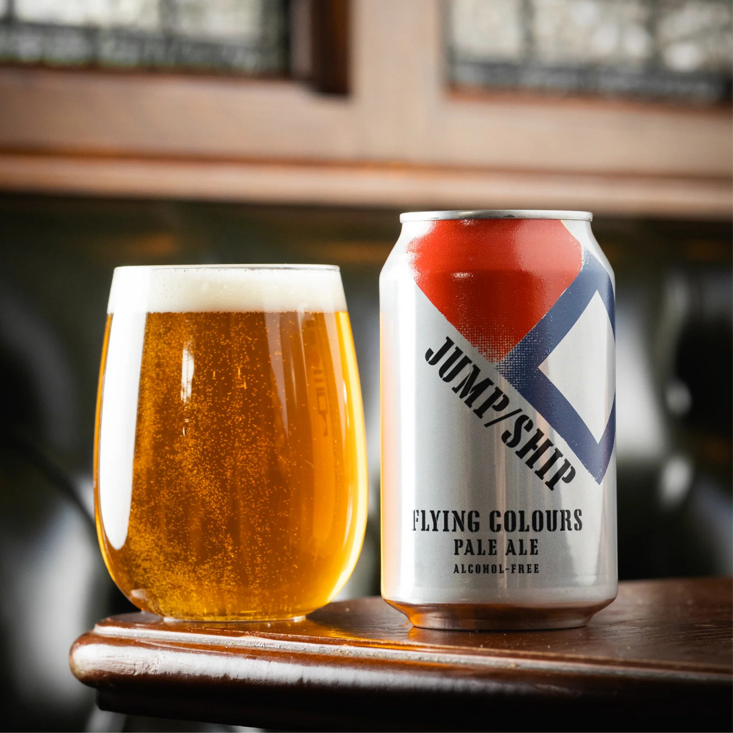 Can of Jump/Ship Flying Colours Pale Ale next to a glass of beer on a wooden surface.