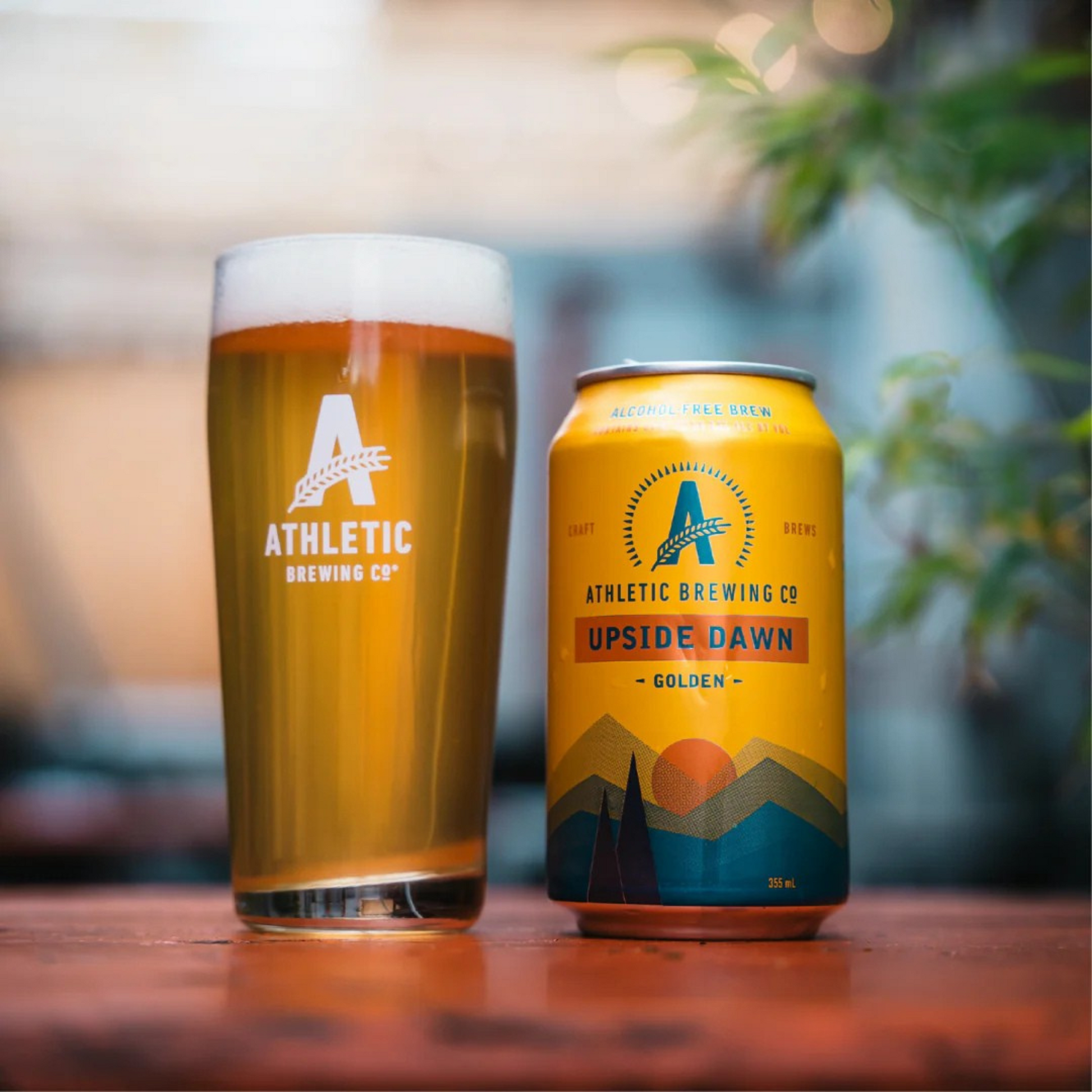 Athletic Brewing Co. beer glass and can on a wooden table with a blurred background